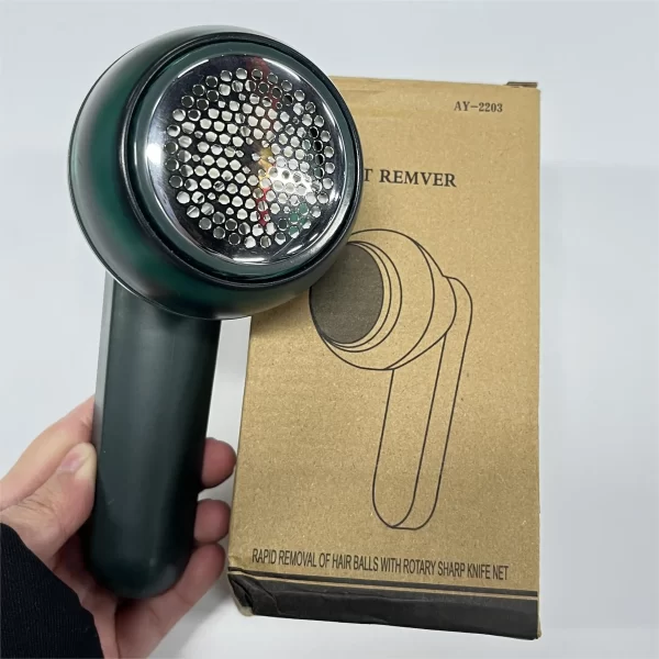 Mašinica za uklanjanje dlačica sa tkanine u zelenoj boji pored katroneske kutije proizvoda